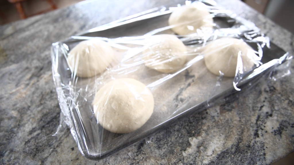 pizza dough balls in baking sheet covered to rest